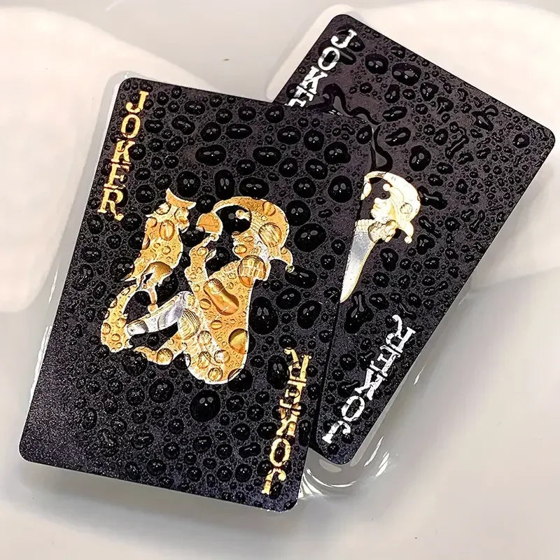 A set of black and gold waterproof playing cards featuring the Joker and Ace of Spades.
