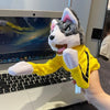 A plush puppet of a husky wearing a yellow outfit with black accents sitting on a laptop keyboard.
