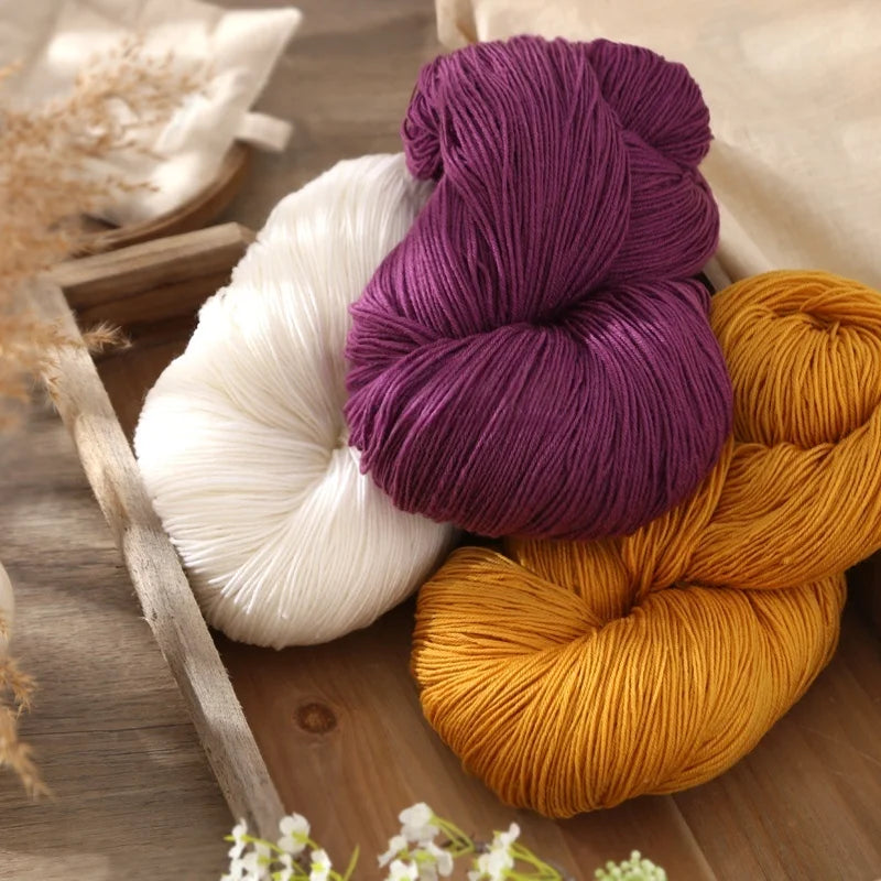 A collection of three skeins of purple, cream, and orange alpaca blend yarn on a wooden surface.