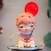 A collectible figure of a pink-haired monster with red hair and large eyes, sitting on a silver base.