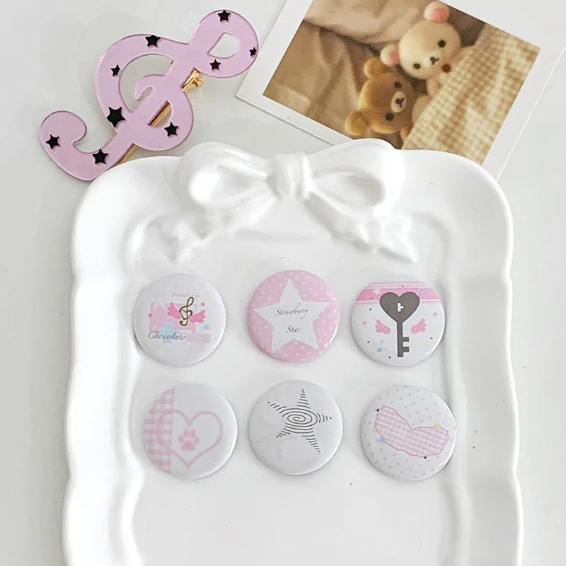 A white tray holds a set of kawaii mini pin badges featuring symbols like a musical note, a star, a key, a paw print, and a b