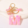 Gold initial heart keychain featuring a butterfly charm and pink tassel on a white background.