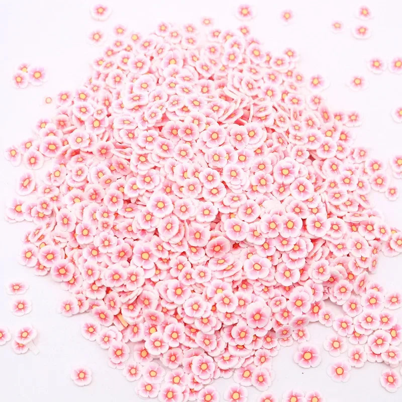 A pile of small pink and white polymer clay flower charms for DIY crafts