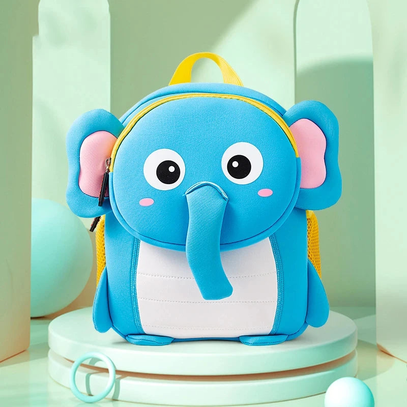A bright blue elephant 3D animal kids backpack with pink ears and yellow accents sitting on a white stand.