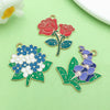 Two enamel flower charms, one red rose and one purple flower, are displayed on a light green surface.