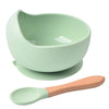 A light green silicone snack cup with a lid and a matching wooden spoon.