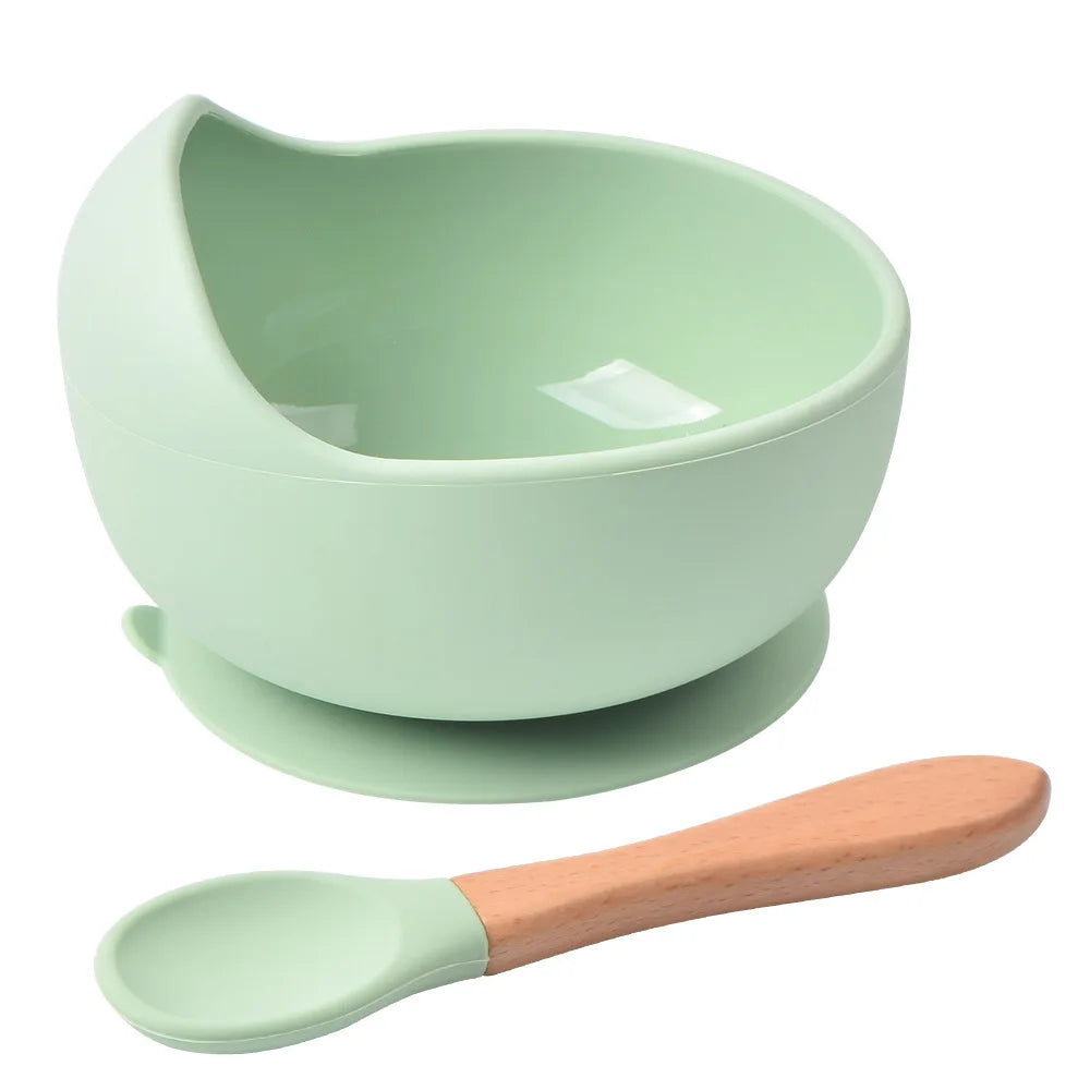 A light green silicone snack cup with a lid and a matching wooden spoon.