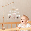A wooden felt forest animal crib mobile hanging above a baby in a crib.