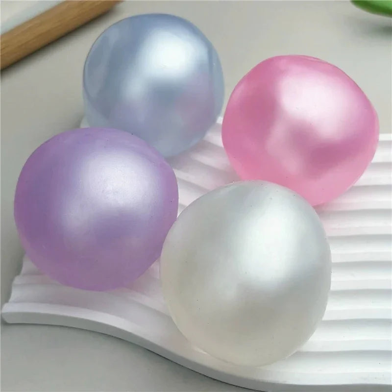 A collection of smooth, iridescent, spherical fidget balls in shades of blue, pink, purple, and white resting on a white surf