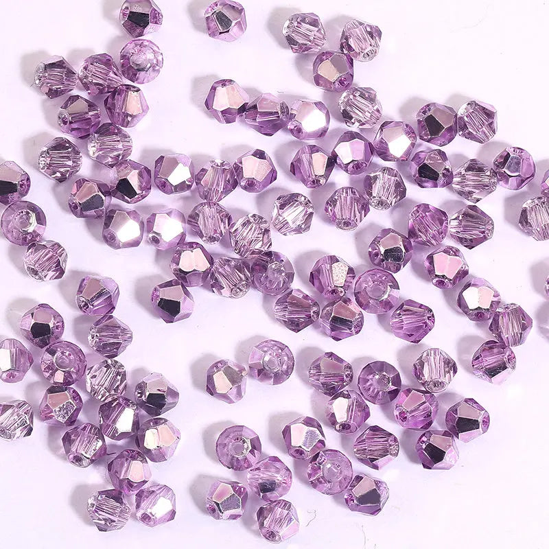 A pile of small, faceted purple crystal bicone glass beads for jewelry making.