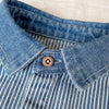 Close-up of a blue and white striped denim shirt with a collar and button detail.