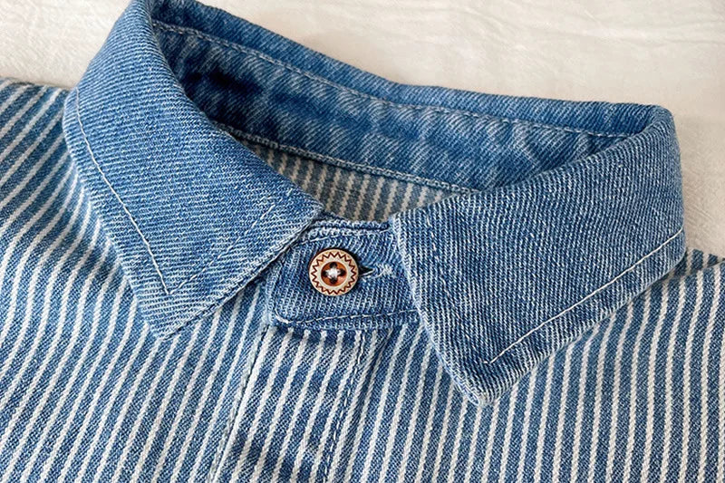 Close-up of a blue and white striped denim shirt with a collar and button detail.