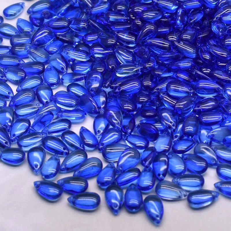 A close-up view of small, brilliant blue water drop Czech glass beads for jewelry making.