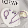 A set of five purple amethyst jewelry pieces including a necklace and earrings displayed on a white ceramic dish.