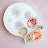 White silicone molds shaped like roses in various shades of pink and peach are displayed on a light pink surface.