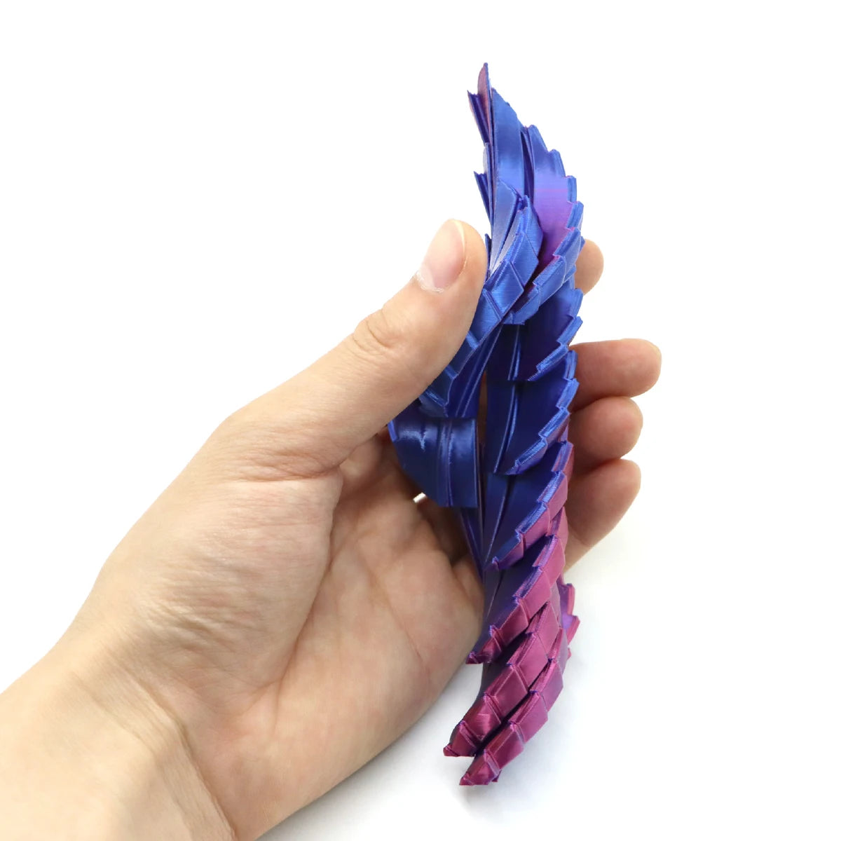 A hand holds a purple and pink expandable dragon egg fidget toy with iridescent, layered plastic wings.