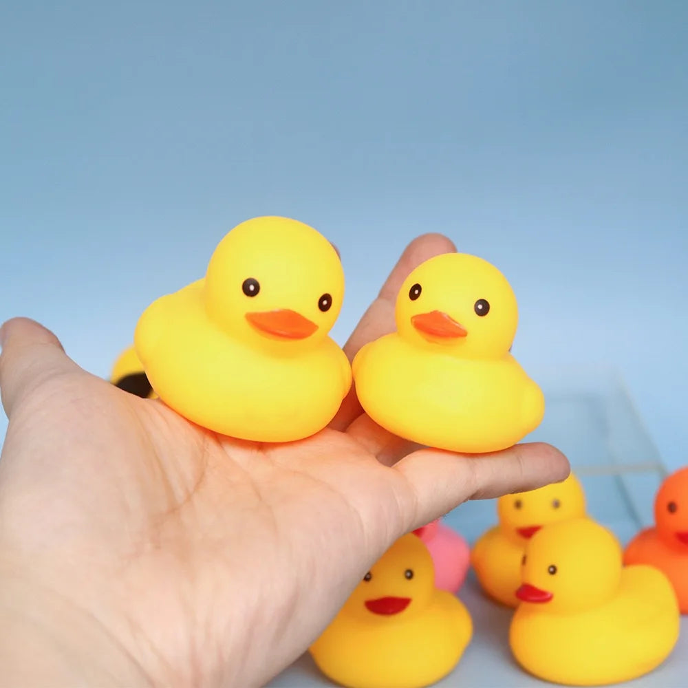 A hand holds several bright yellow silicone duck bath toys against a light blue background.