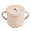 A beige silicone snack cup with a lid and handle, featuring a decorative cutout design.