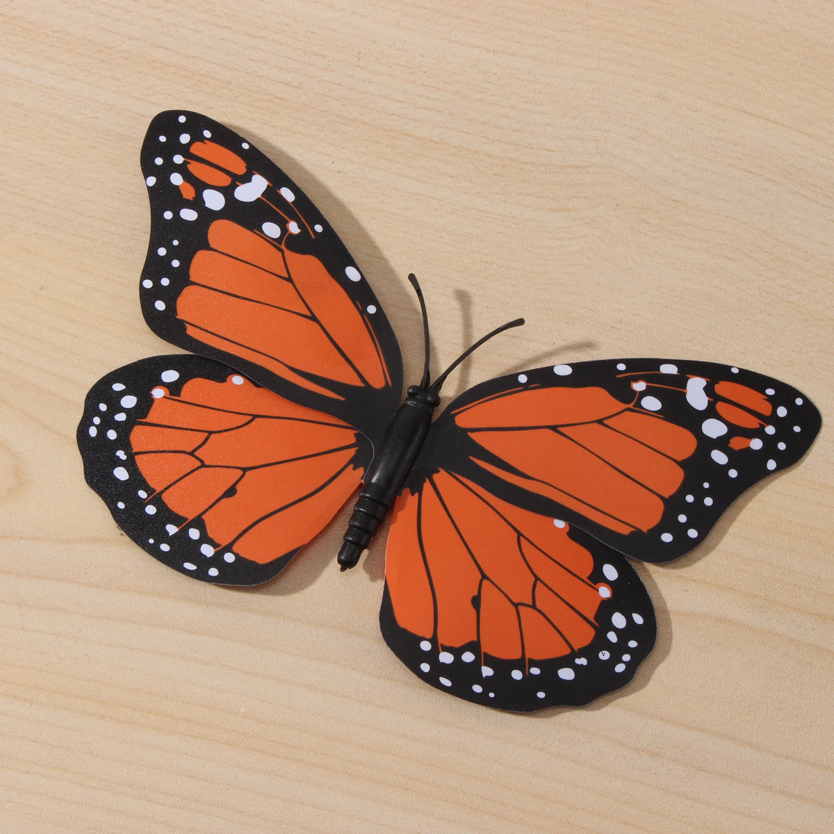 Décoration de papillon monarque orange et noir avec des taches blanches, sur une surface en bois clair.
