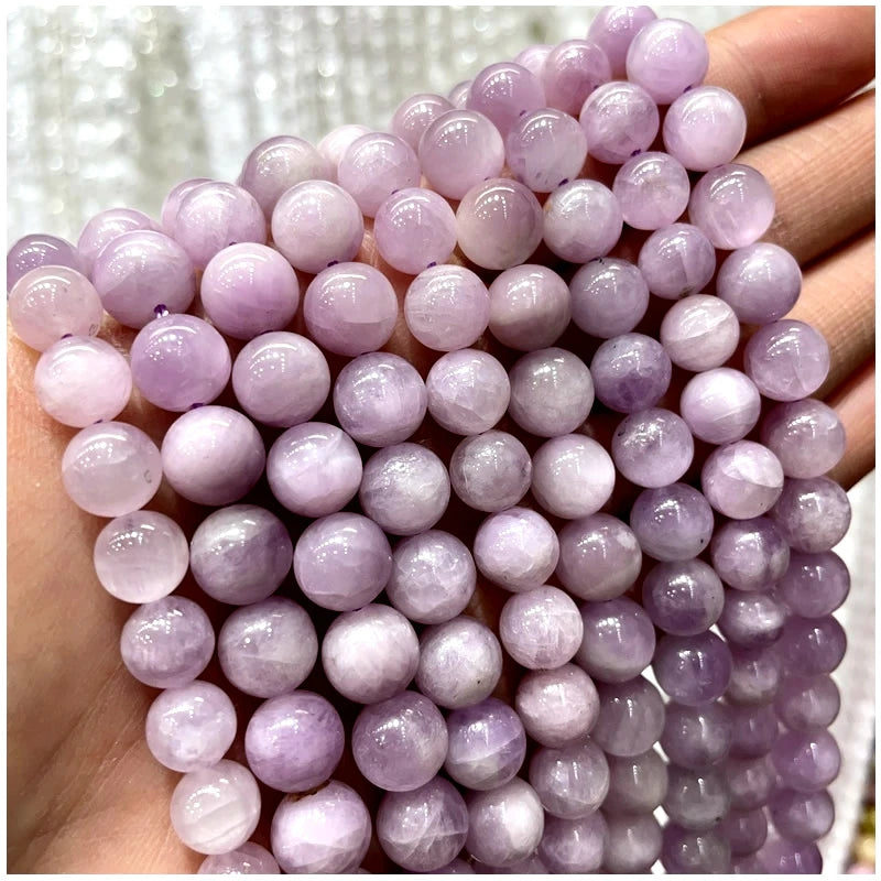A hand holds a strand of round purple amethyst and garnet beads for DIY jewelry making.