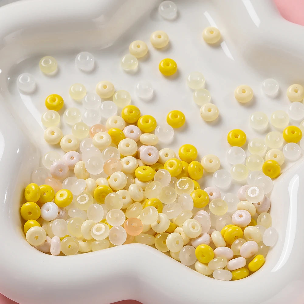 A close-up view of a pile of small glass spacer beads in various shades of yellow, white, and pink.
