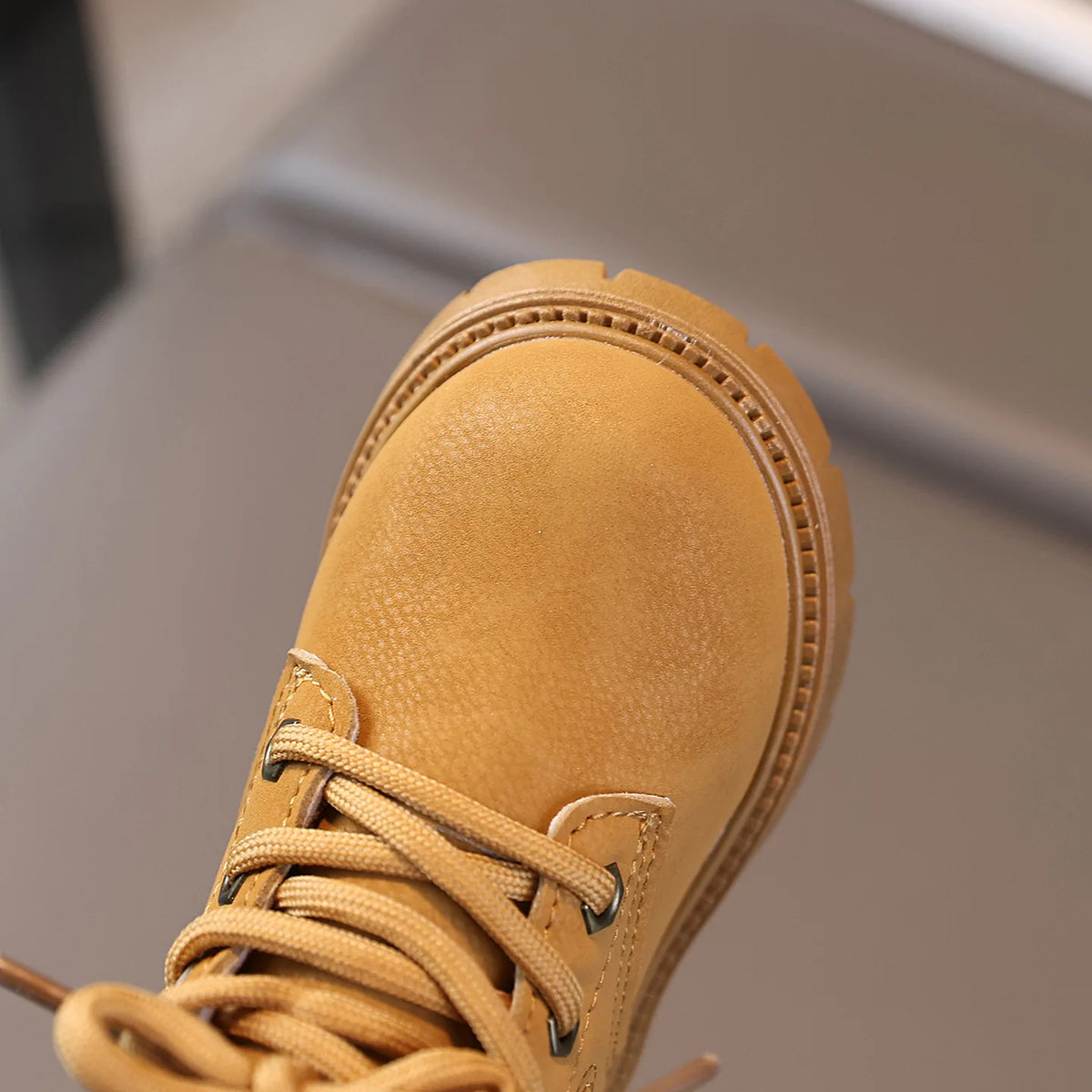 A close-up view of a tan kids' winter leather boot with laces and stitching.