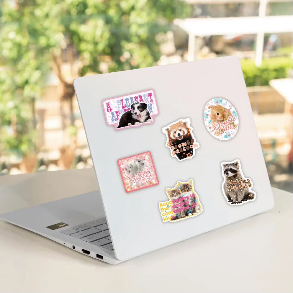 A laptop is shown with various cute retro cartoon stickers featuring cats and other animals on the lid.