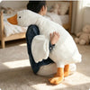 A child is holding a white goose plush toy with orange beak and feet on a light carpet.