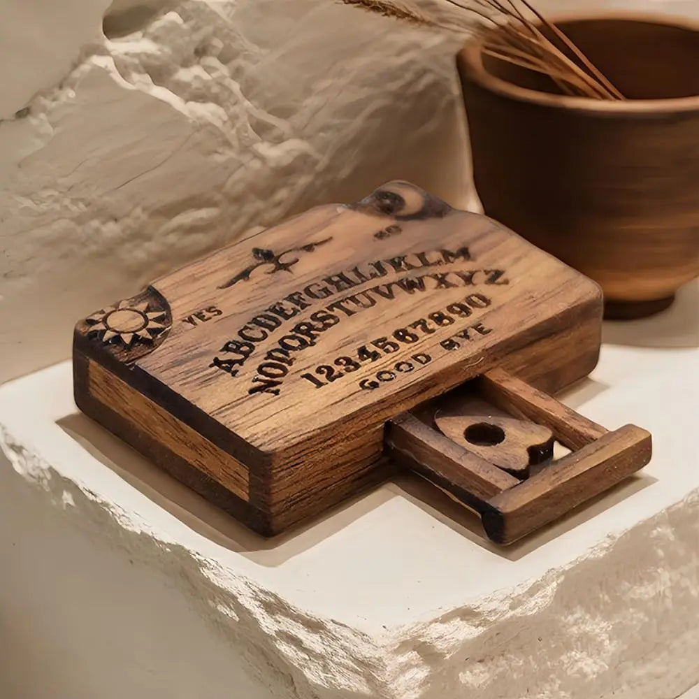 A wooden miniature Ouija board with a drawer is displayed on a white stone surface.