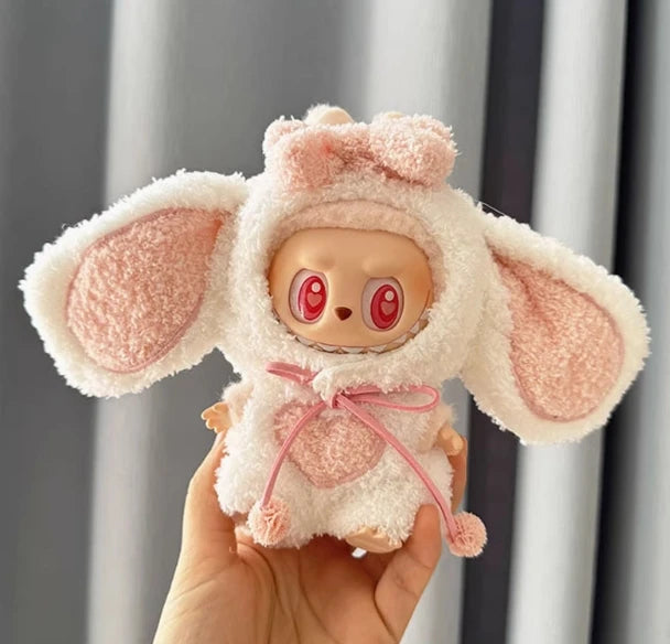 A soft pink fluffy rabbit costume for a doll with large ears and expressive eyes is held in a hand.