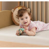 A baby is playing with a wooden toy on a light-colored surface in a nursery setting.