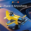 A yellow solar powered rotating airplane dashboard ornament placed on a blue car interior surface.