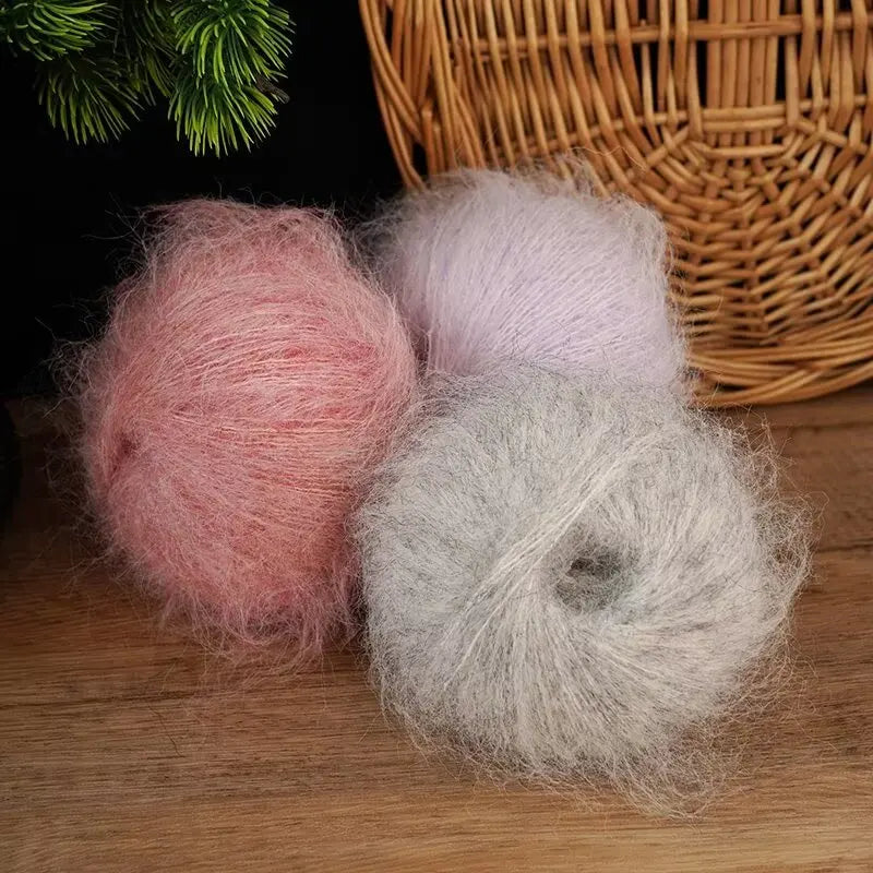 Three balls of pink and gray long-haired alpaca blend yarn resting on a wooden surface next to a wicker basket.