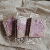 A clear plastic package containing a pack of rainbow textured paper for junk journals and collage art resting on a light fabr