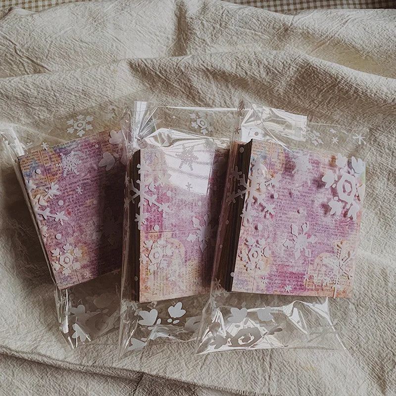 A clear plastic package containing a pack of rainbow textured paper for junk journals and collage art resting on a light fabr