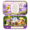 A purple tin box containing a miniature dollhouse scene with a cottage and flowers.