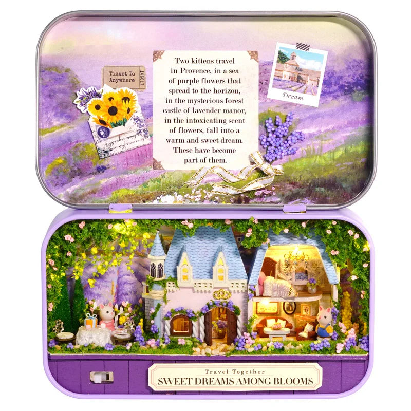 A purple tin box containing a miniature dollhouse scene with a cottage and flowers.