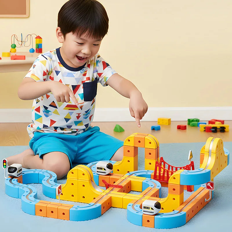 A child is playing with a yellow and orange magnetic 3D cube train set featuring flexible tracks on a blue surface.