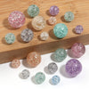 A collection of round loose glitter cracked acrylic beads in various shades of pink, green, and purple scattered on a wooden 