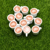 A collection of small, round, pink-colored wax melts or charms arranged on green grass.