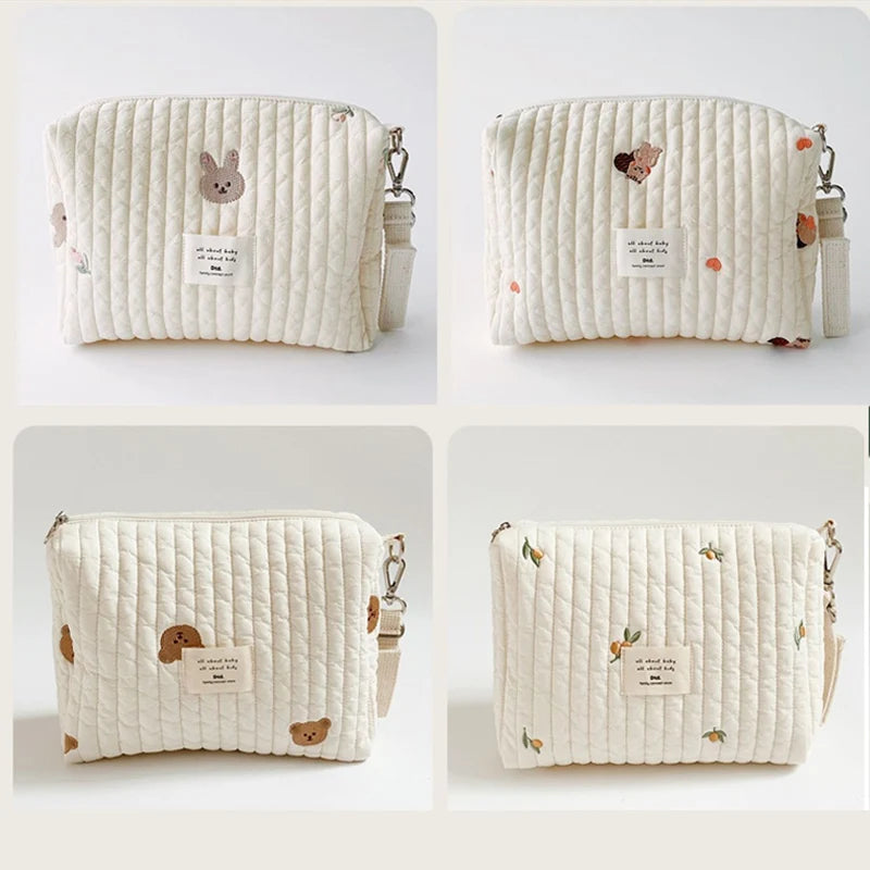 A cream quilted baby diaper caddy organizer with small animal embroidery and attached stroller straps.