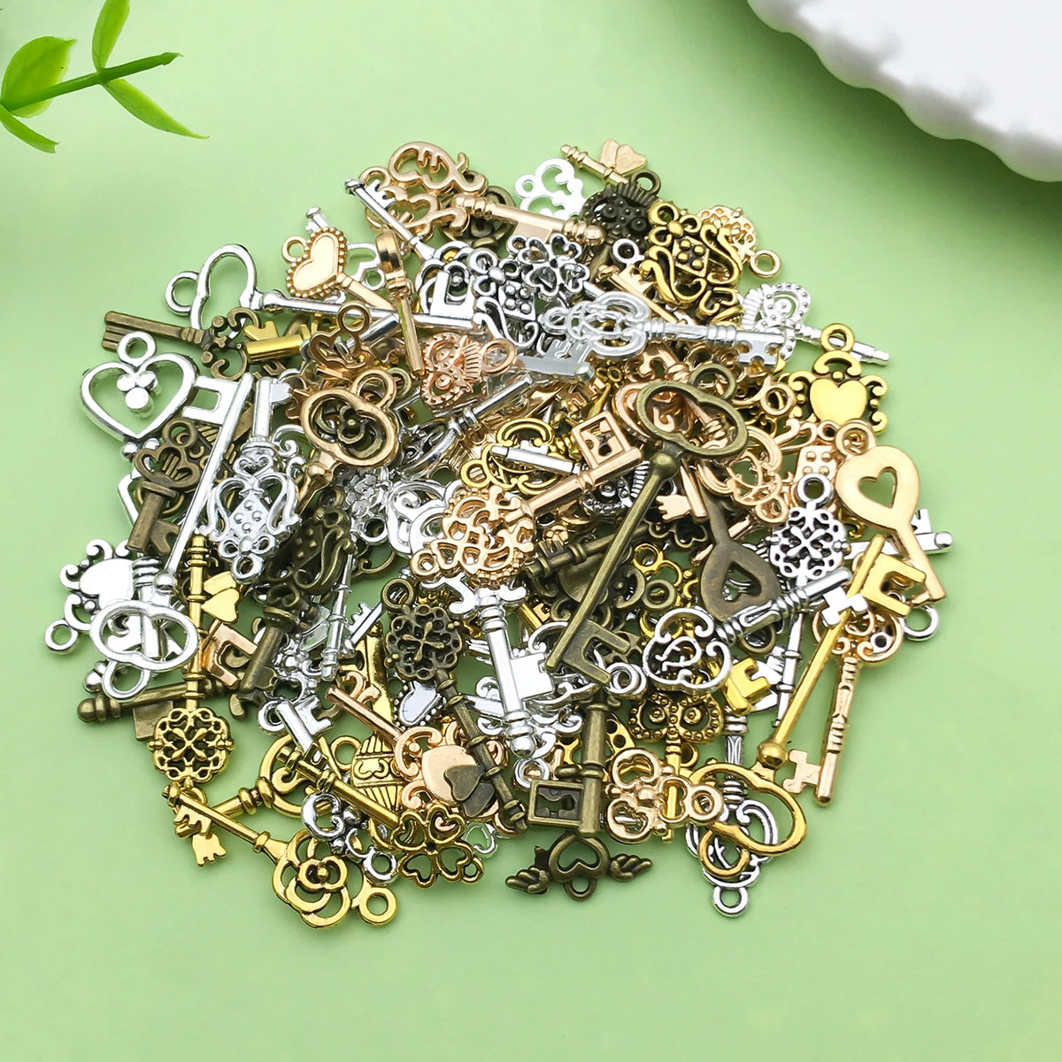 A pile of vintage brass and silver key charms for jewelry making scattered on a light green surface.