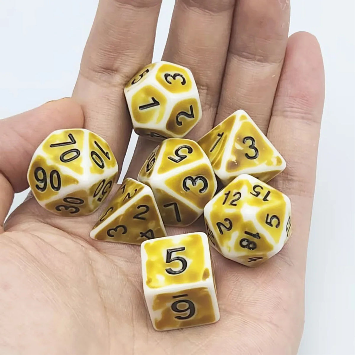 A hand holds a set of ten polyhedral dice with yellow and white markings on a white background.