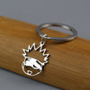 Silver keychain featuring an anime-inspired crown and face design attached to a wooden surface.