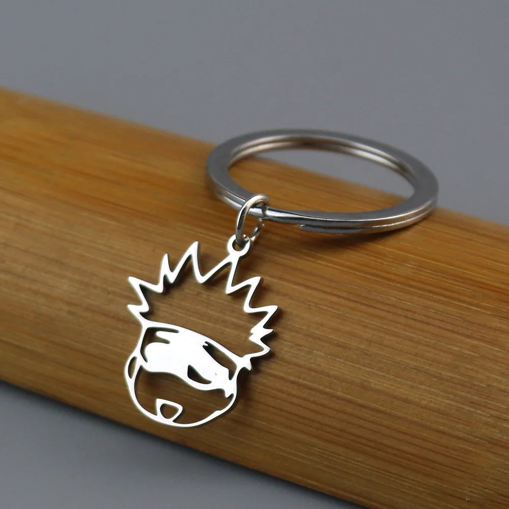Silver keychain featuring an anime-inspired crown and face design attached to a wooden surface.