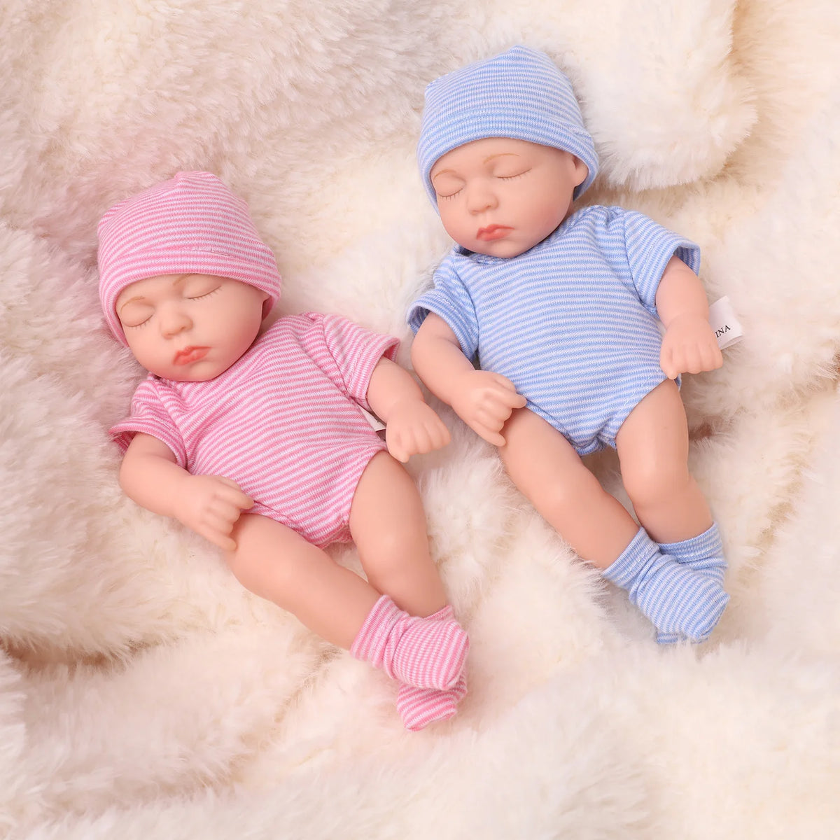 A realistic soft vinyl baby doll with a newborn outfit set, featuring a pink striped top and blue striped hat.
