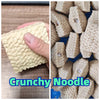A close-up of a light beige crunchy noodle stress relief squishy toy being held by a hand.
