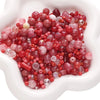 A pile of multicolor glass beads in shades of pink, red, and clear are displayed in a white dish.