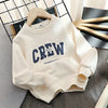 A cream-colored kids cotton pullover sweatshirt with navy blue crew lettering displayed on a wooden hanger.