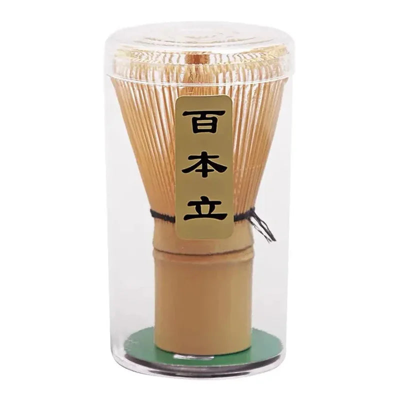 A clear glass container holding a traditional bamboo matcha whisk set with a wooden base.